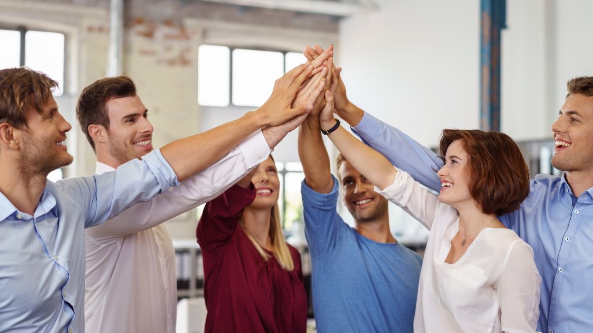 Personengruppe steht im Kreis und schlägt in der Mitte ein.