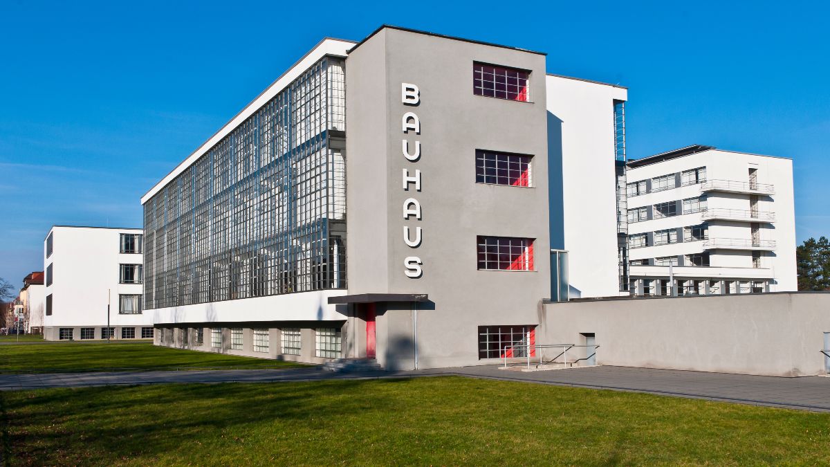 Fassade des modernen Bauhaus-Gebäudes mit großen Glasflächen, klaren horizontalen und vertikalen Linien sowie glatter Beton- und Stahlstruktur.